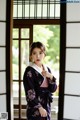 A woman in a purple kimono standing in front of a window.