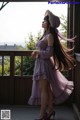 A woman in a purple dress and hat standing on a porch.