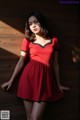 A woman in a red dress leaning against a wooden wall.