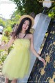 A woman in a yellow dress and straw hat posing for a picture.