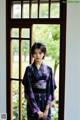 A woman in a kimono standing in front of a window.