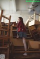 A woman in a school uniform standing on a pile of wooden chairs.