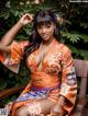 A woman in an orange kimono sitting on a wooden chair.